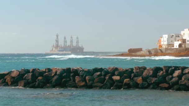 Piattaforma di produzione petrolifera nell'oceano. Un argine in pietra nel mare e diverse case in primo piano. Il concetto di inquinamento, riscaldamento globale ed emissioni di carbonio — Video Stock