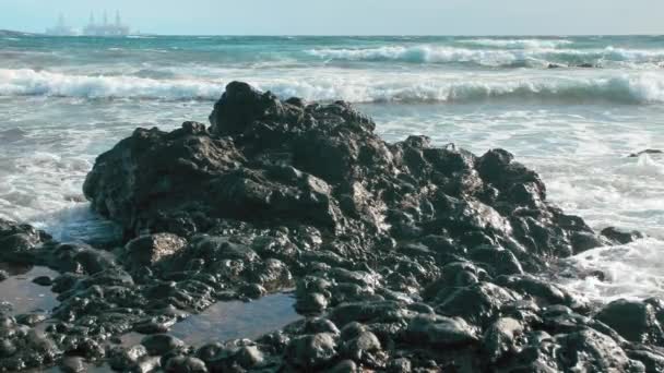 Una piedra de lava en el océano. Torres para la producción de plataformas petrolíferas en segundo plano. El concepto de protección del medio ambiente y contaminación oceánica — Vídeo de stock