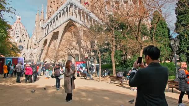 Βαρκελώνη, Ισπανία - Φεβρουάριος 2019: Sagrada Familia Cathedral By Gaudi. Ασιάτες τουρίστες από την Κίνα ή την Ιαπωνία τραβήξτε φωτογραφίες κοντά στην έλξη. χρήση smartphone — Αρχείο Βίντεο