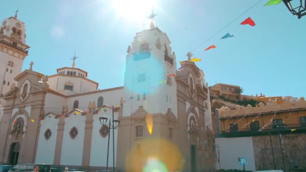 Kathedraal in de Spaanse stad. De stralen van de zon schijnen in het frame, de straat is versierd met feestelijke vlaggen. Het concept van de lichte religie — Stockvideo