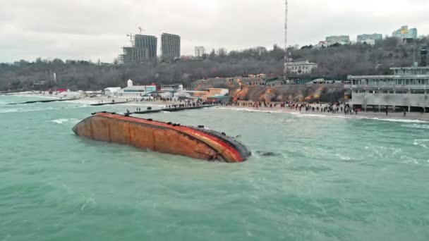 Odessa, Ucrânia - novembro de 2019: Um desastre ambiental. Muitas pessoas na praia tiram fotos de um navio-tanque que encalhou e capotou a bordo durante uma tempestade severa. tiro drone aéreo — Vídeo de Stock