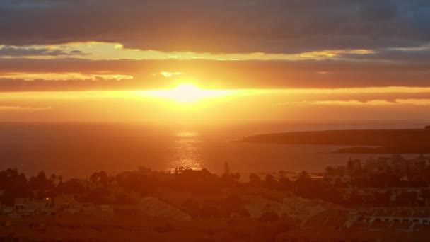 Orange solnedgång över havet. Färgglada solstrålar och bländning vid solnedgången eller gryningen över staden nära havet, Stor skiva sol och dramatiska moln — Stockvideo