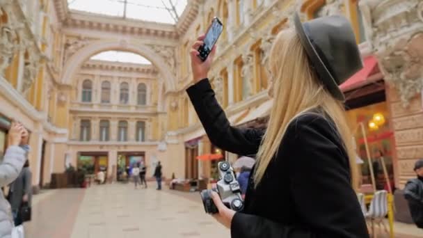 Odessa, Ukrajina - listopad, 2019: Mladý kavkazský blogger s retro filmovou kamerou v ruce fotí na svém chytrém telefonu. Koncept nové generace technologií, retro a moderních kamer — Stock video