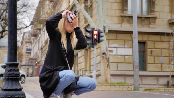 A young Caucasian hipster woman takes a picture on a vintage retro film camera. Crossroads road and traffic lights in the background. The concept of street photography on film equipment — Stock Video