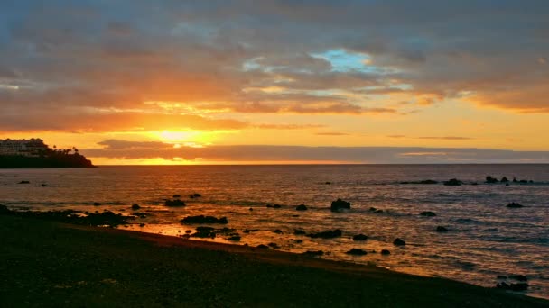 Барвистий яскравий драматичний захід сонця, світанок на океані. Сонце піднімається з-за горизонту, освітлює море променями. Різнокольорове небо оранжеве, жовте, рожеве і синє — стокове відео