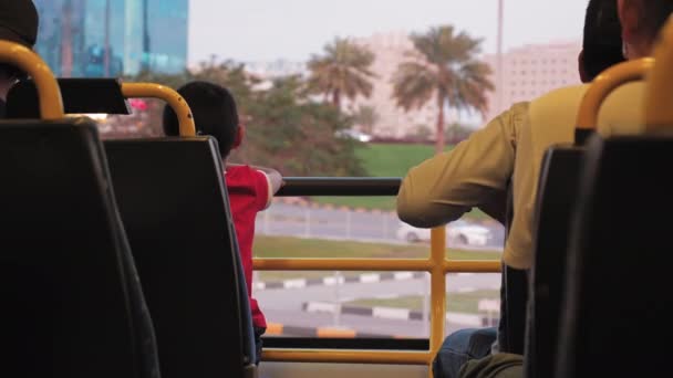 Ismeretlen fiú ül az ablak mellett egy emeletes modern buszon. Pálmafák és elhaladó autók a háttérben. Egyesült Arab Emírségek, Dubai — Stock videók