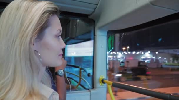 若いブロンドの女性は夜の大都市を通って2層バスに乗っています。道路やヤシの木の背景にあります。ドバイ,アラブ首長国. — ストック動画
