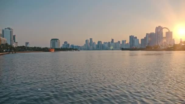 Pôr-do-sol ou amanhecer numa metrópole. Casas altas, arranha-céus contra o sol laranja. Uma água, lago em primeiro plano. Pode ser usado para ilustrar capitais, grandes cidades e construção de arranha-céus — Vídeo de Stock