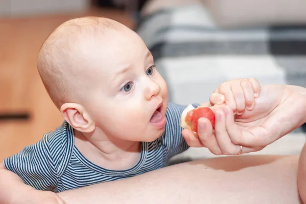 Kleinkind isst mit Mamas Händen einen Pfirsich. Stockfoto