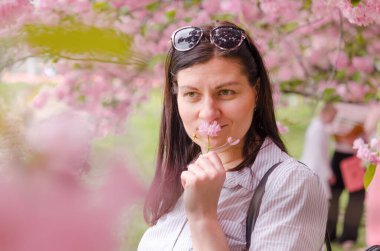 Genç beyaz bir kız kiraz çiçeklerinin aromasının ve güzelliğinin tadını çıkarıyor. Doğu Avrupa 'daki Dnipro Ukrayna şehir parkında kiraz çiçeği.