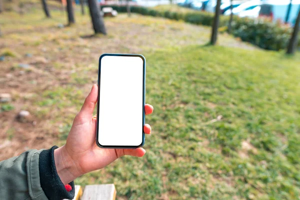 Main tenant le téléphone blanc d'écran blanc avec l'écran blanc extérieur — Photo