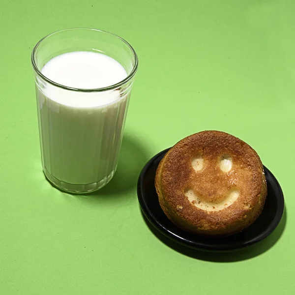 a glass of milk with a donut with a smiley face on a green background