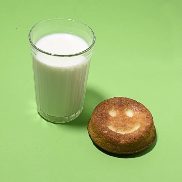 a glass of milk with a donut with a smiley face on a green background