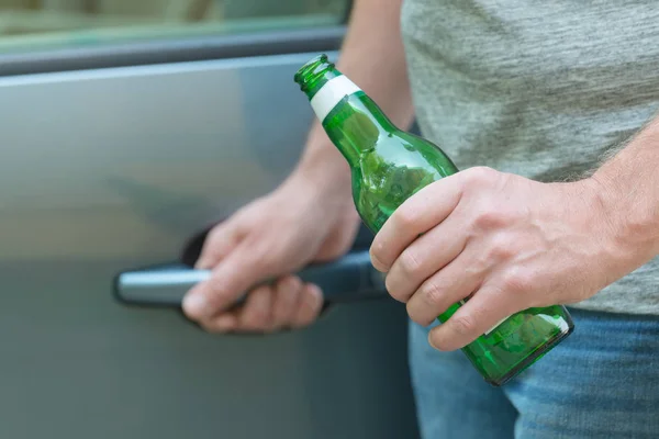 Человек открывает свою машину, держа в руках бутылку пива — стоковое фото