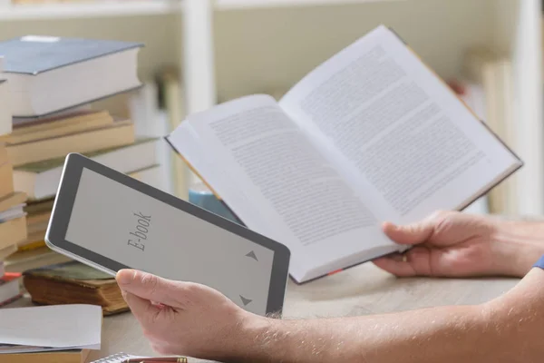 Man håller en modern eboksläsare och boken i biblioteket — Stockfoto