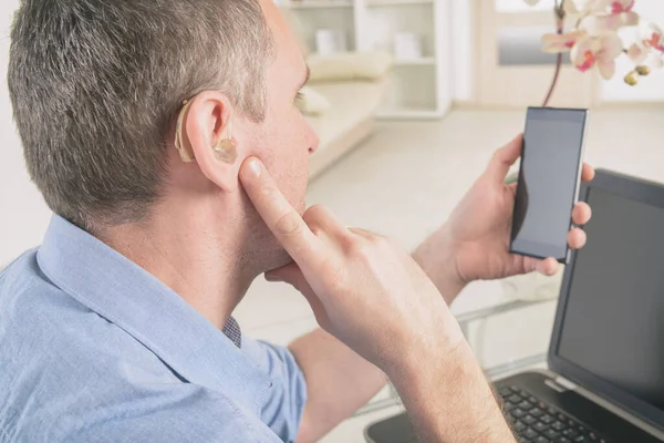 Uomo con problemi di udito che lavora con laptop e telefono cellulare — Foto Stock