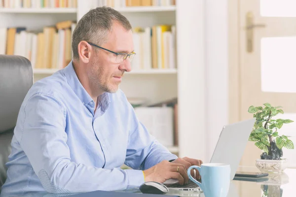 Hombre trabajando en su computadora portátil en la oficina en casa — Foto de Stock