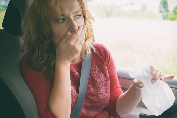 Woman suffering from motion sickness in a car and holding sick bag