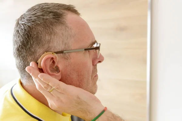 Man wearing deaf aid in ear attempting to hear something