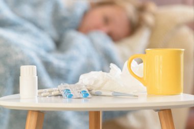 Grip veya soğuk algınlığı ndan muzdarip kadın ne yazık ki yatağında bir battaniye ile kaplı yatıyor. İlaçlar, ilaçlar, bardak ve dokular ön planda