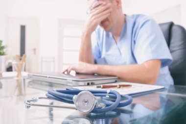 Çok çalışan doktor ofisinde oturuyor. 