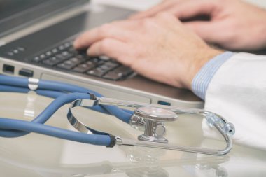 Doktor el ön planda stetoskop ile bir dizüstü bilgisayarda yazarak yakın çekim