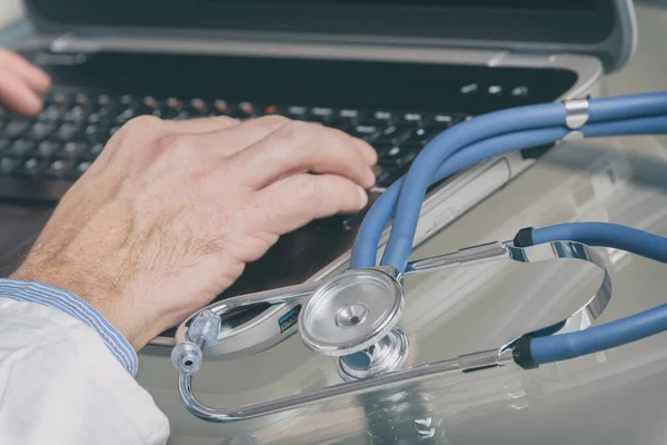 医生的手用听诊器在前台在笔记本电脑上打字的特写 — 图库照片