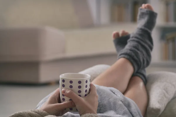 Sıcak Bir Bardak Içeceği Ayakları Yastığın Üzerinde Uzanan Bir Kadın — Stok fotoğraf