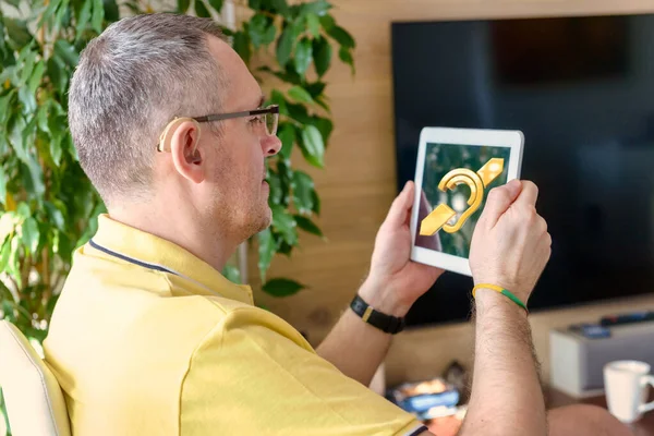 Man wearing deaf aid in ear with tablet showing deaf sign an the display. Concept of using tablets and smartphones by deaf and with hearing impairment people