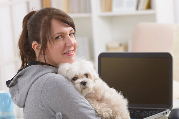 Hearing impaired woman working on laptop with her dog in hands at home office
