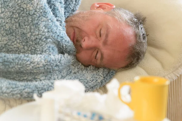 患有流感或感冒的人不幸地躺在床上 身上覆盖着一条毯子 前景药物 杯子和组织 — 图库照片