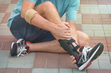 Spor ayakkabılı, ayak bileği ortozu ya da diş teli takan bir adam.