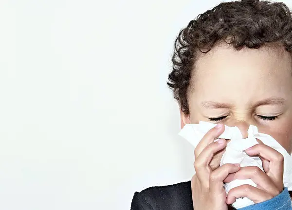 Boy blowing nose after catching a cold on white background