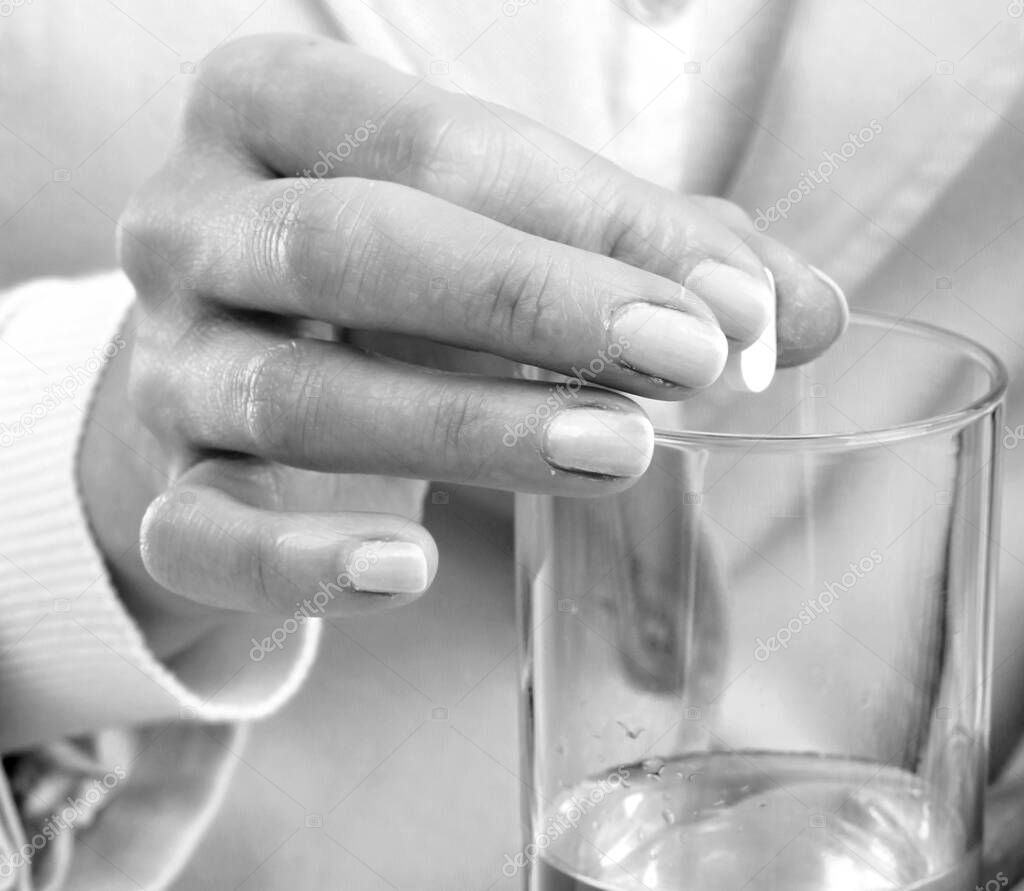 woman taking contraceptive pill with a glass of water in her hand on white background