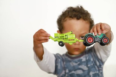 Küçük çocuk beyaz arka planda oyuncak traktörüyle oynuyor.