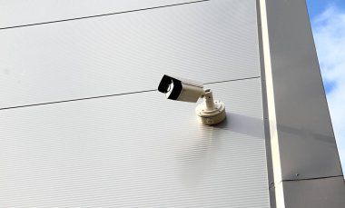 Bir binaya bağlı metal bir direğin üzerindeki sanayi bölgesine bakan güvenlik kamerası.