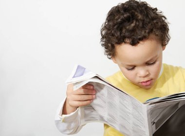 Çocuk gazete okuyor ve gazeteye bakıyor. Beyaz bir geçmişi var. 