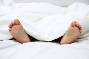 Ayaklar yatak örtülerinden sarkıyor.