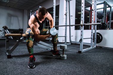 Bankta oturan bir spor salonunda dumbbells ile eller için egzersizleri yapıyor atlet