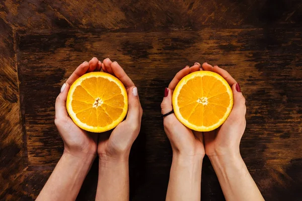 Duas meninas segura em suas mãos laranjas metade sobre mesa de madeira — Fotografia de Stock