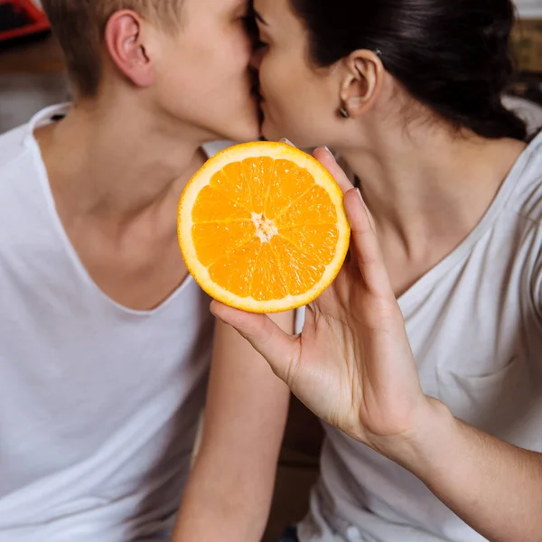 Любовники целуются и держат апельсин в руках — стоковое фото