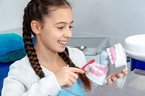 Fille dans le bureau du dentiste montre comment se brosser les dents — Photo