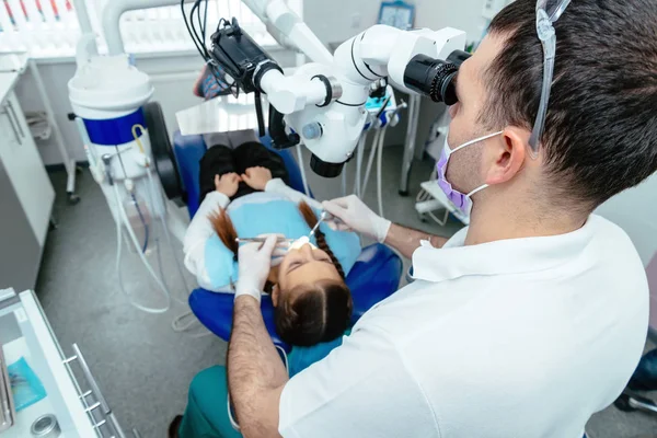 Der Zahnarzt untersucht die Zähne des Kindes mit dem Mikroskop. professionelle zahnmedizinische Geräte — Stockfoto