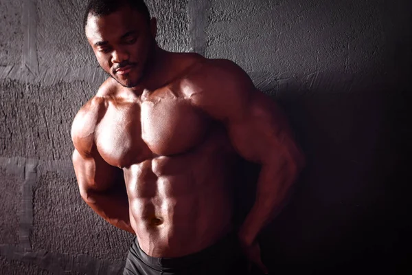Bodybuilder se tient appuyé sur le mur. Athlète masculin afro-américain posant démontrant le développement musculaire — Photo