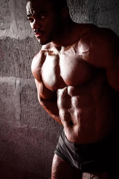 El culturista está apoyado en la pared. Atleta masculino afroamericano posando demostrando desarrollo muscular — Foto de Stock