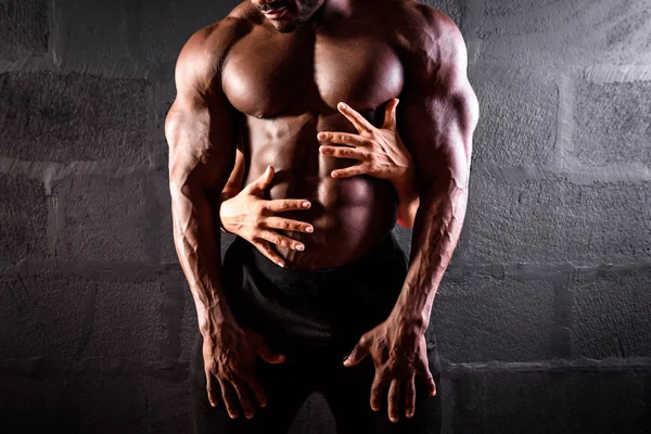 African American male athlete posing showing developed musculature with girl hands on his abdominal muscles — Stock Photo, Image