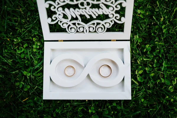 Anillos de boda en una caja blanca especial con la inscripción boda en hierba verde. Disparo desde arriba —  Fotos de Stock