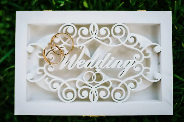 Свадебные кольца в специальной белой коробке с надписью свадьбы на зеленой траве. Выстрел сверху — стоковое фото