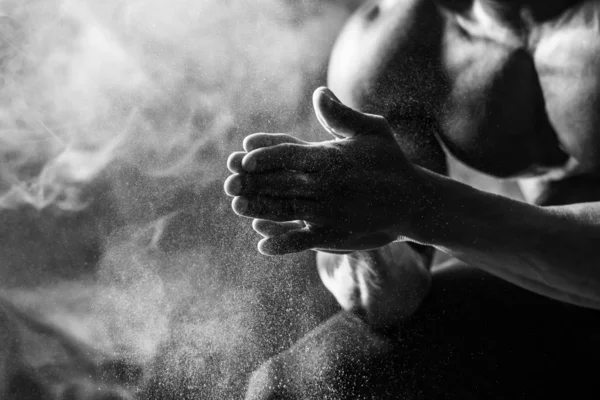 Бодібілдер використовує магнезію рук. Чоловік сидить на чорному тлі з димом. Чорно-білий постріл — стокове фото