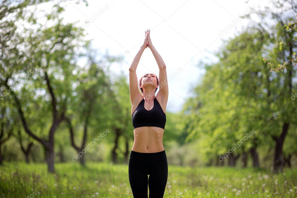 Young beautiful girl practices yoga in a green park in nature